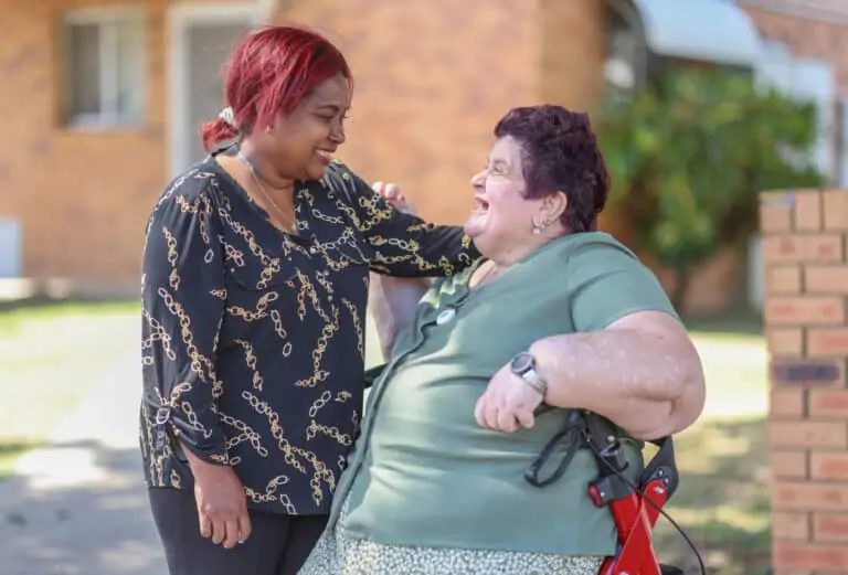 Woman sitting on a walker talking to woman with red hair, both are smiling