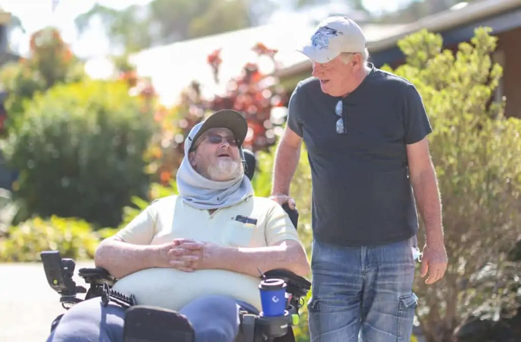 Two men chatting together, one is in a wheelchair, the other is showing personal care