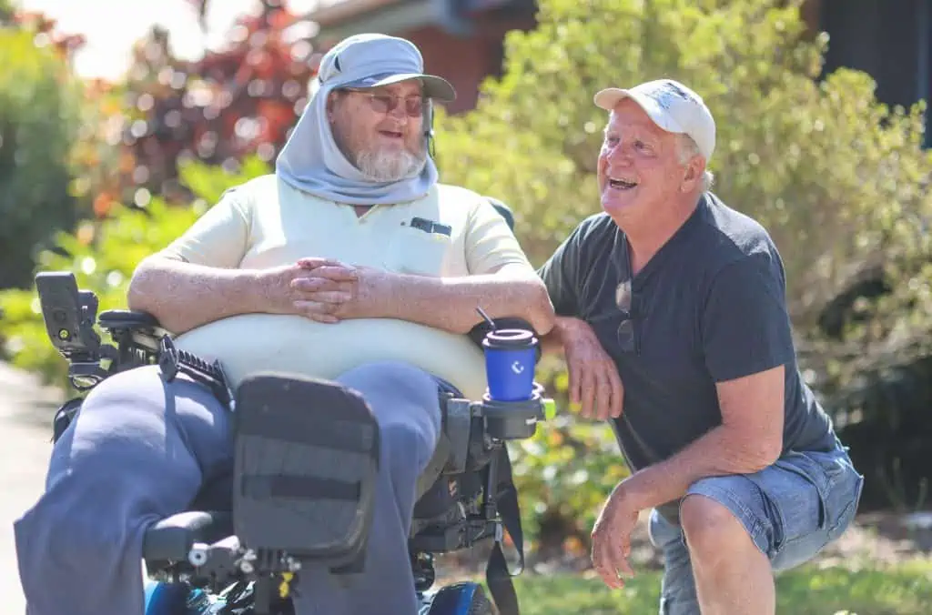 Two men laughing together, one is in a wheelchair demonstrating supported independent living
