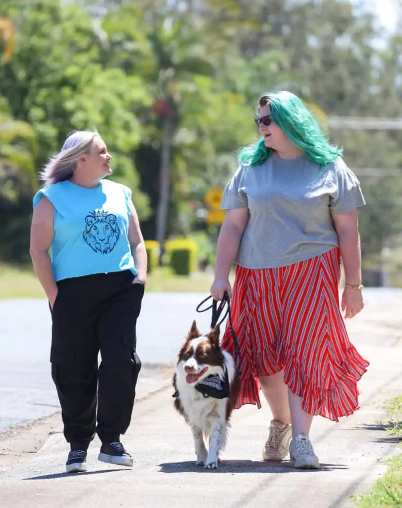 Two women walking next to each other, one is walking a support dog next to her