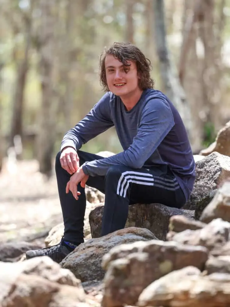 Young man sitting on rocks and smiling to the camera.